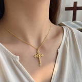 Gold cross pendant necklace worn at the collarbone