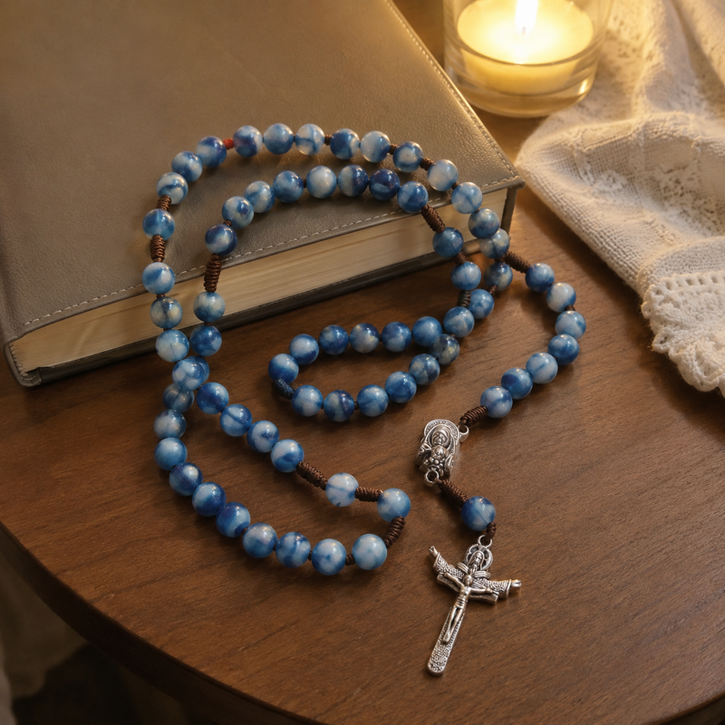 Blue Catholic rosary beside a prayer book and candle