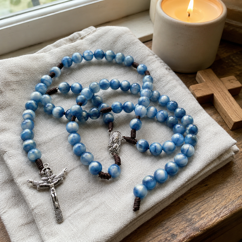 Blue Catholic rosary arranged beside a candle and wooden cross